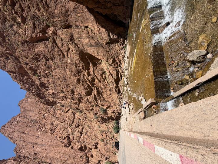 Steep red canyon walls of Todra Gorge with a shallow stream and small visitors below