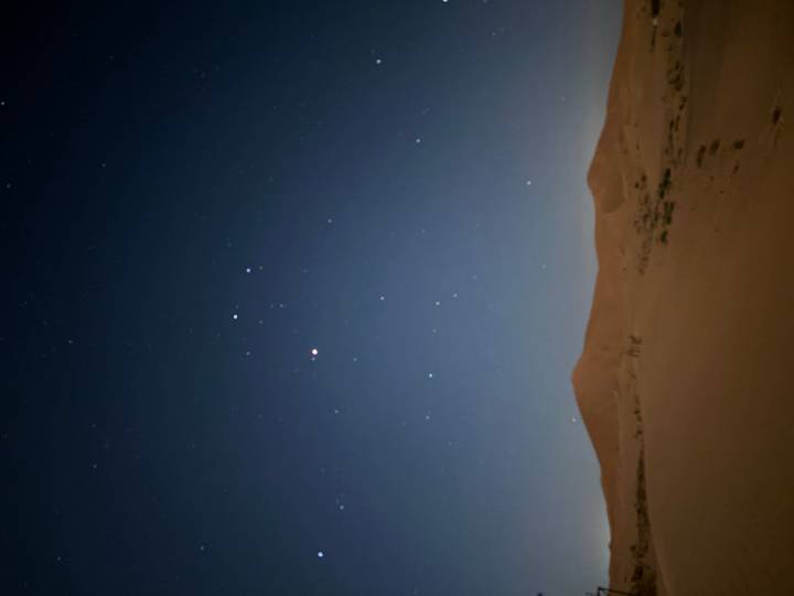 Night desert scene with a starry sky above dark sand dunes