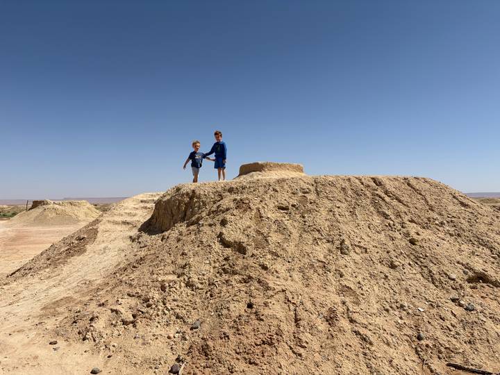 Two children stand atop an eroded desert mound under a clear blue sky