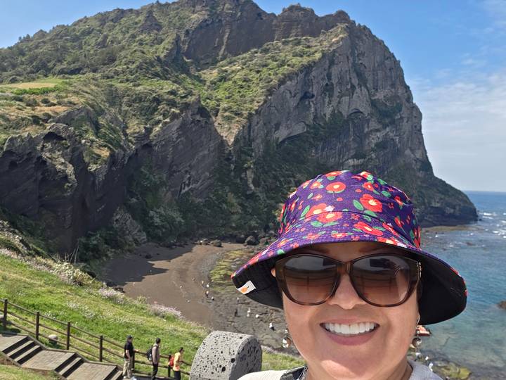 Traveler’s selfie with dramatic coastal cliffs and blue sea behind on Jeju Island.