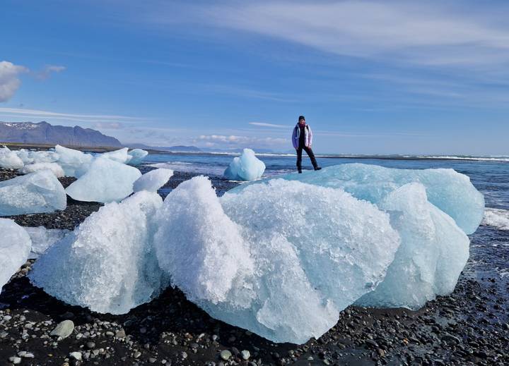 Traveler standing atop sparkling ice fragments on a black sand beach with mountains beyond