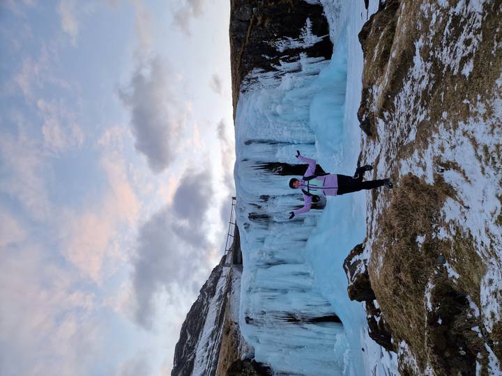 Excited visitor posing in front of an icy waterfall with pastel evening sky