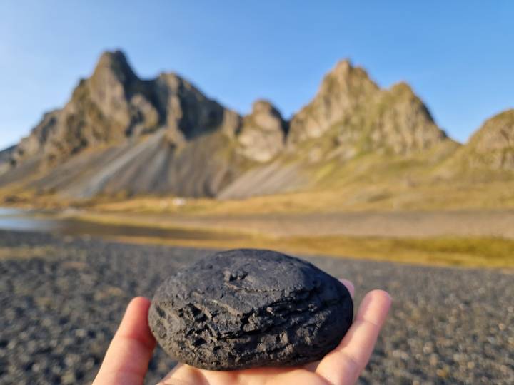 Hand holding a smooth black volcanic stone with blurred mountain backdrop