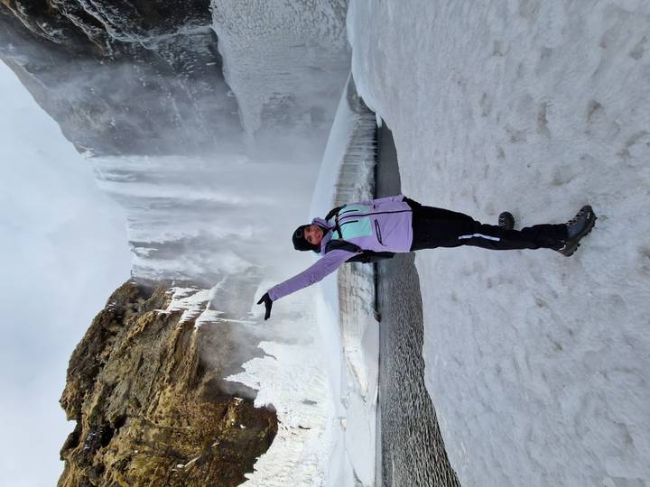 Traveler in winter gear celebrating before a partially frozen waterfall and snowfield