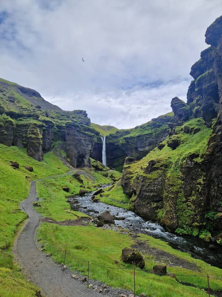 Tall slender waterfall plunging into a lush green canyon with a stream winding below