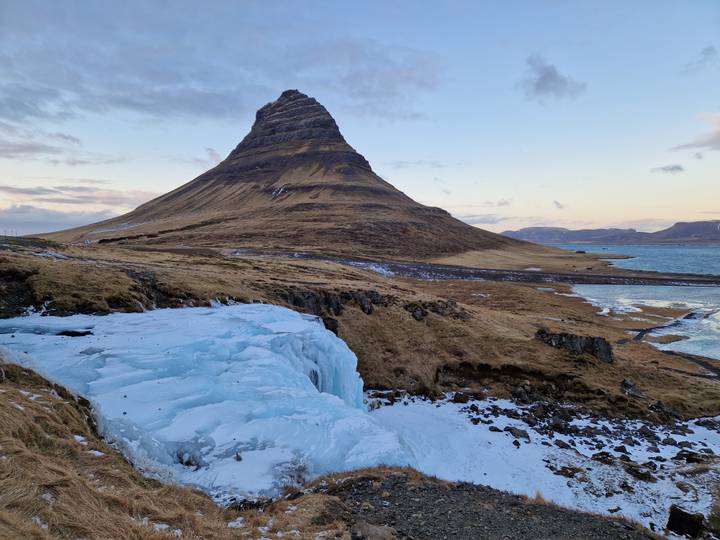 Iconic cone-shaped Kirkjufell mountain beside a partially frozen cascade at dusk