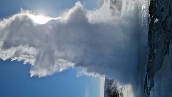 Powerful geyser eruption shooting high into the sky with sunlight shining through spray