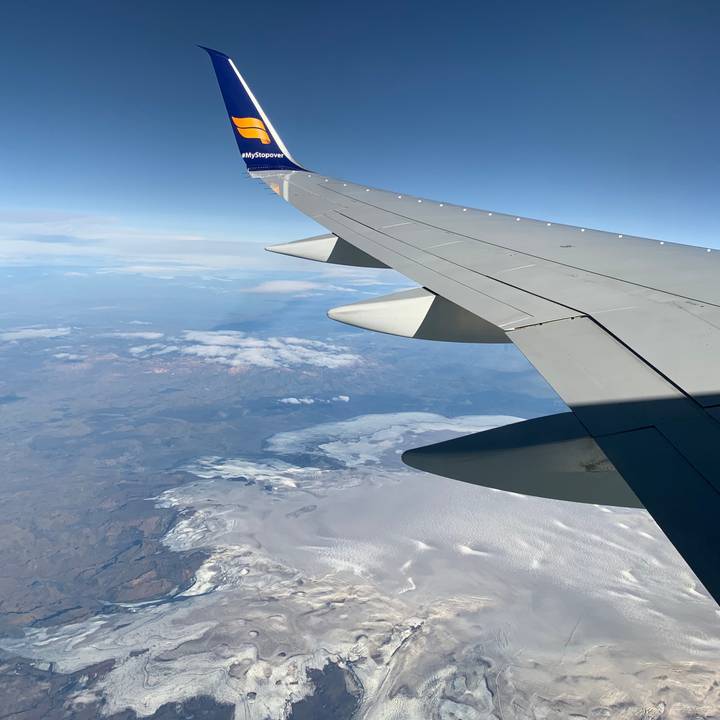 View from airplane window of wing over snow-covered landscape and scattered clouds