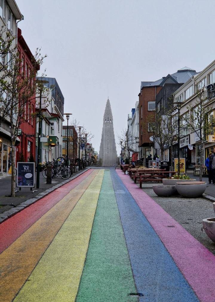Colorful rainbow-painted street leading to Hallgrimskirkja with shops and a few pedestrians on a misty day.
