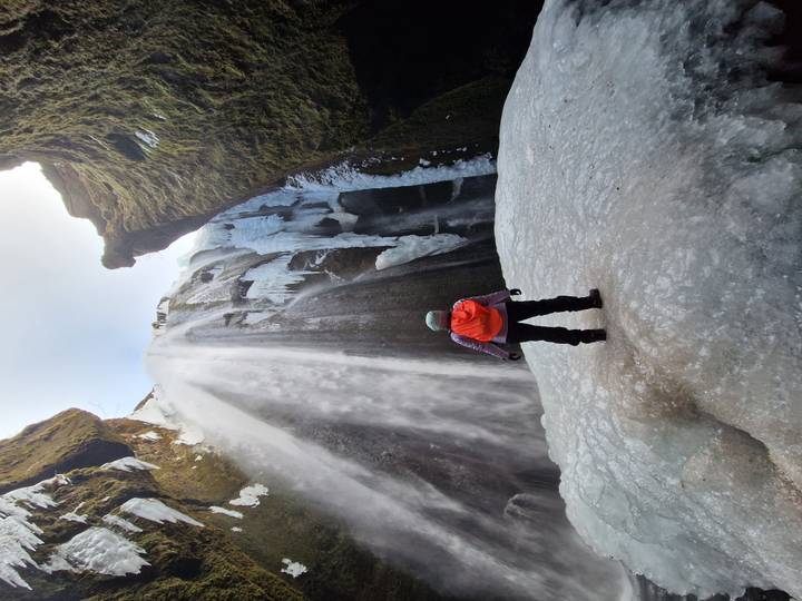 Adventurer stands on ice at the base of a towering frozen waterfall inside a steep gorge.
