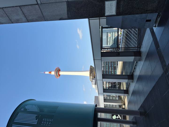 Kyoto Tower rises into a clear blue sky as seen from a modern urban terrace.