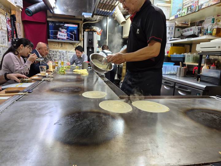 Chef prepares hot pancakes on a teppan grill while diners enjoy food at a cozy eatery.
