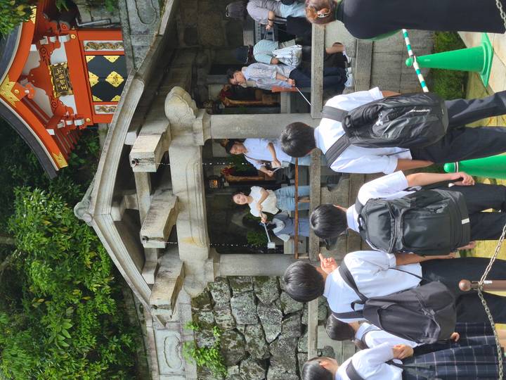 Students queue to drink sacred water at a temple pavilion ornamented with dragons.