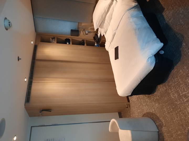 Compact hotel cabin with neatly made bed, wooden wardrobe and tablet on duvet.
