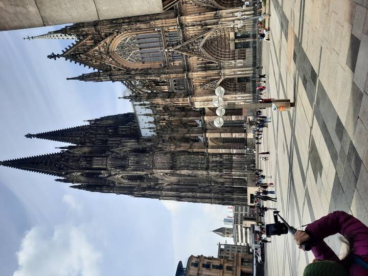 Imposing twin-spired Cologne Cathedral towers over the city square with visitors below.