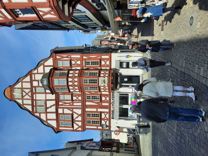 Half-timbered medieval building lines a cobblestone street with tourists walking past.