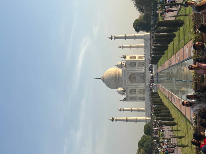 Iconic frontal view of the Taj Mahal with reflecting pool and visitors along the pathway on a clear day.