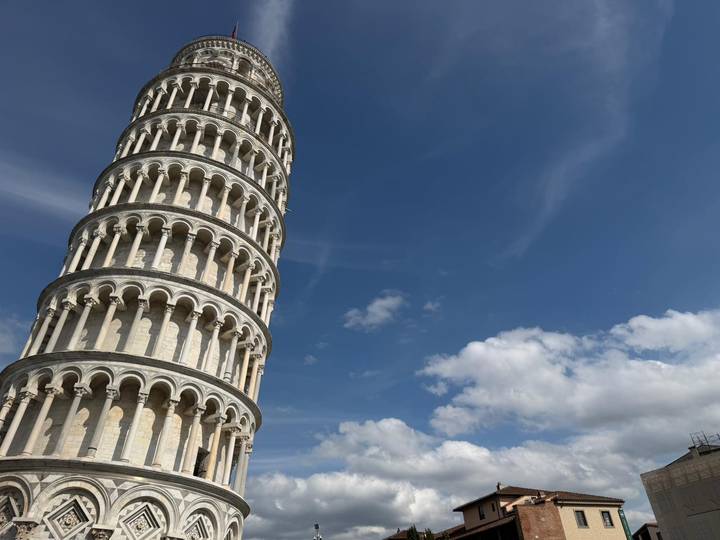 Leaning Tower of Pisa rises on the left with expansive blue sky and wispy clouds filling the frame.