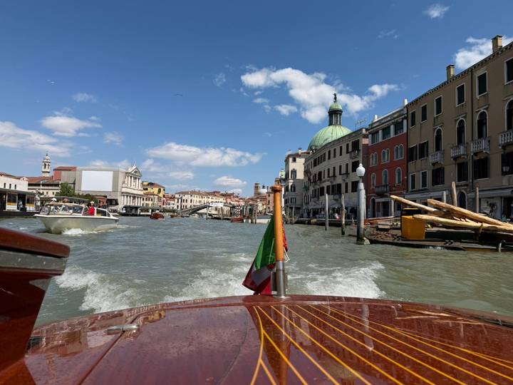 View from a wooden motorboat cruising down Venice's Grand Canal with historic buildings and dome ahead.