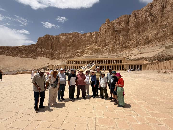 Tour group stands before the temple of Hatshepsut carved beneath towering cliffs.
