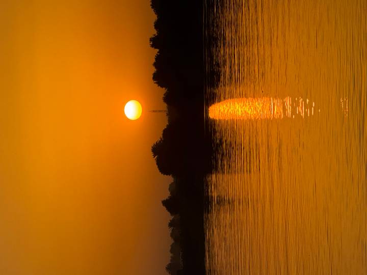 Brilliant orange sun sets over calm Nile waters casting a shimmering reflection.