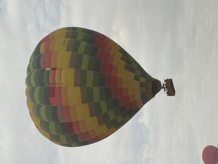 A brightly striped hot-air balloon floats against a lightly clouded sky.