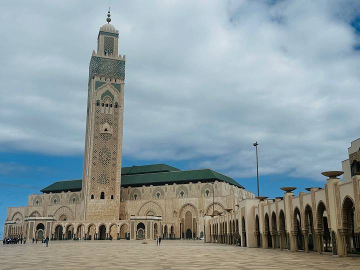 The soaring minaret and green-tiled roof of Casablanca’s Hassan II Mosque stand against a partly cloudy sky.