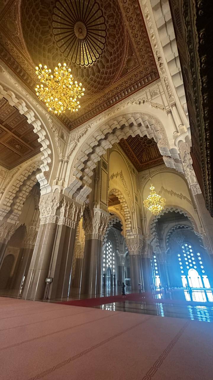 Intricate stucco arches and a sparkling chandelier adorn the interior of a Moroccan mosque or palace.