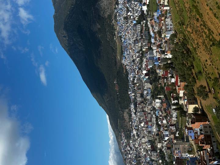 Elevated view of a Moroccan town framed by a forested mountain under a bright blue sky.