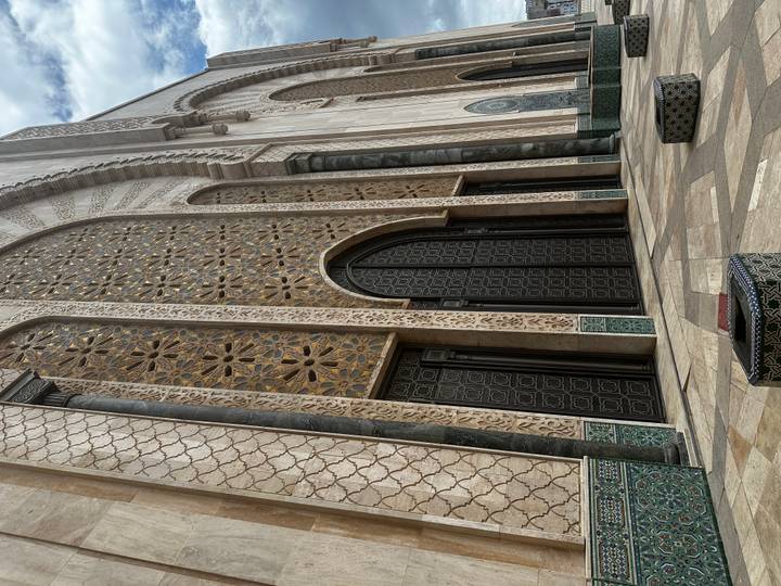 Ornately patterned stone facade and grand arched doors of the Hassan II Mosque in Casablanca.