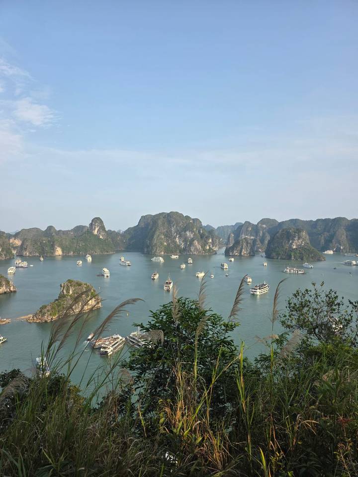 Panoramic view of Halong Bay's limestone karsts dotted with cruise boats under a hazy sky.