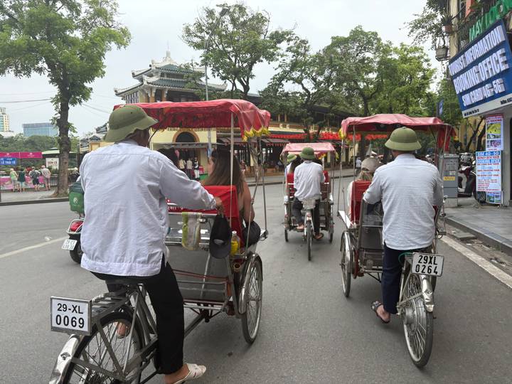 Cyclo drivers pedal tourists through a historic Vietnamese street lined with temples and shops.