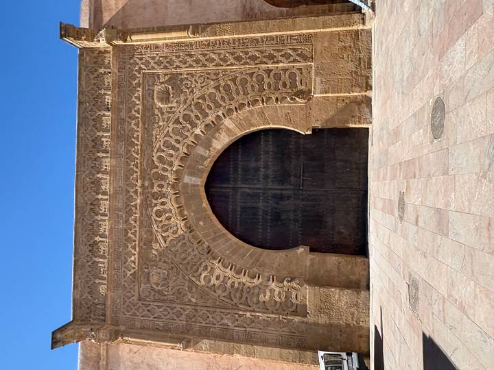Intricately carved sandstone gateway with large arched wooden doors against a clear blue sky