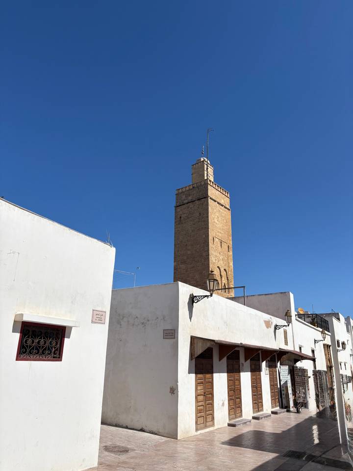 Tall brick minaret rising above white buildings under a clear blue sky