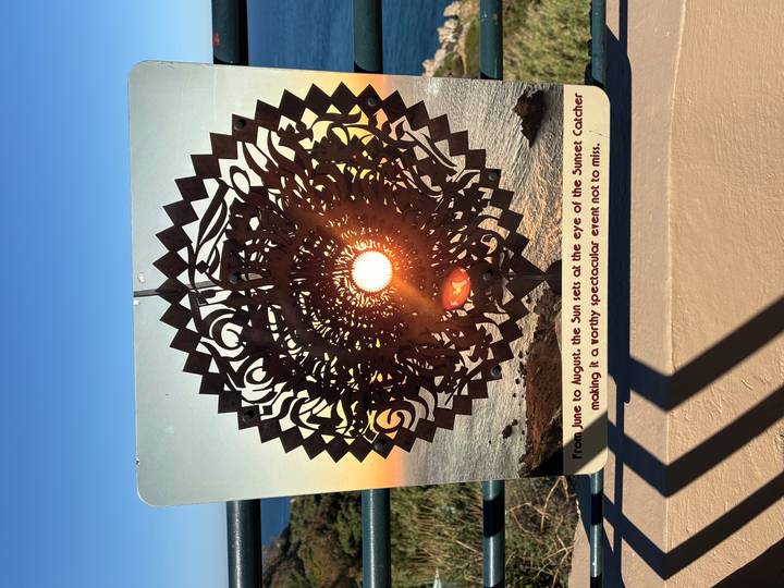 Informational sign featuring a decorative cut-out design with sunset text above the ocean