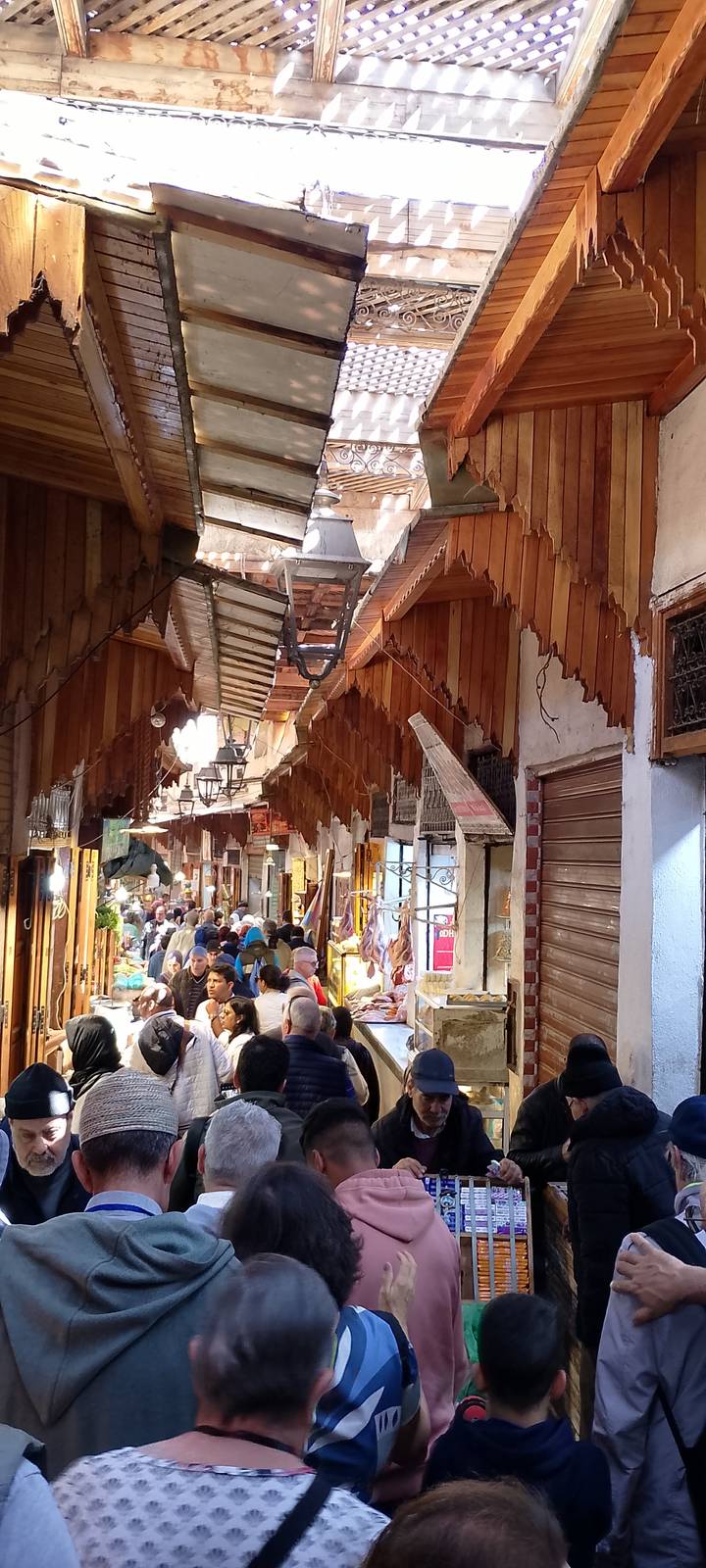 Busy covered souk with wooden eaves and crowds shopping at market stalls