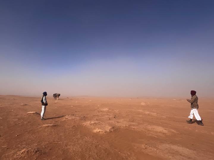 Vast dusty desert landscape with two travelers standing far apart under a clear blue sky.