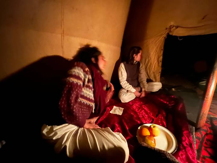 Blurred low-light scene of travelers sitting inside a tent on red carpets with fruit nearby.