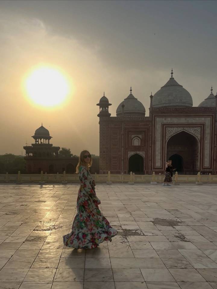 Soft sunrise light over ornate red sandstone mosque next to the Taj Mahal complex with visitors in foreground.