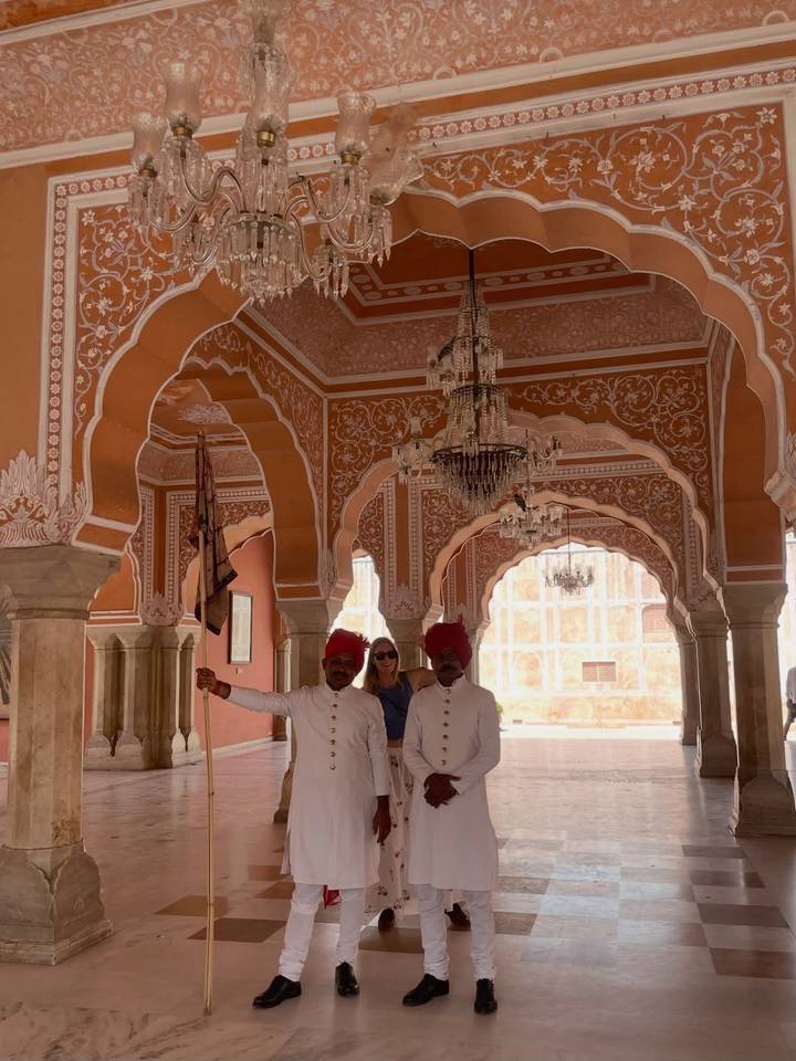 Ornate pink archways with two uniformed guards and a tourist standing inside a historic palace hall.