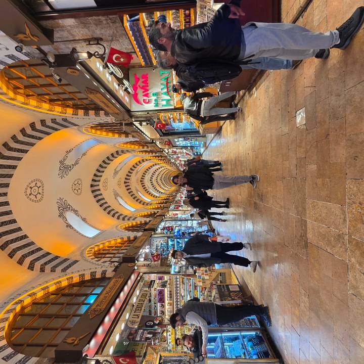 A bustling indoor bazaar with arched, ornate ceilings lit in warm tones; shoppers wander between colorful stalls.