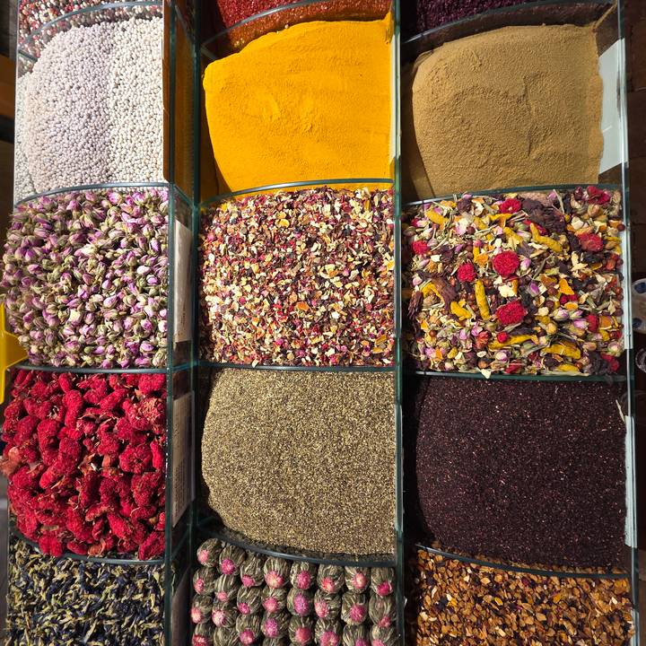 Colorful rows of dried herbs, teas, and spices neatly displayed in glass bins at a market stall.