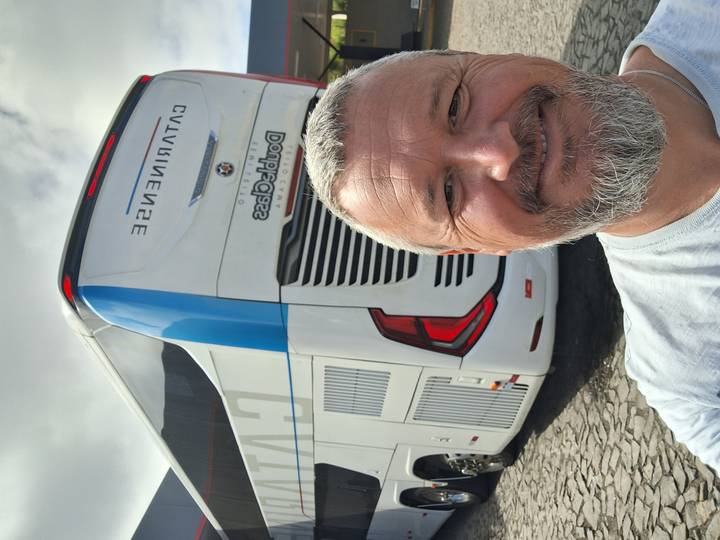 Smiling man takes a selfie with a modern touring coach parked behind him