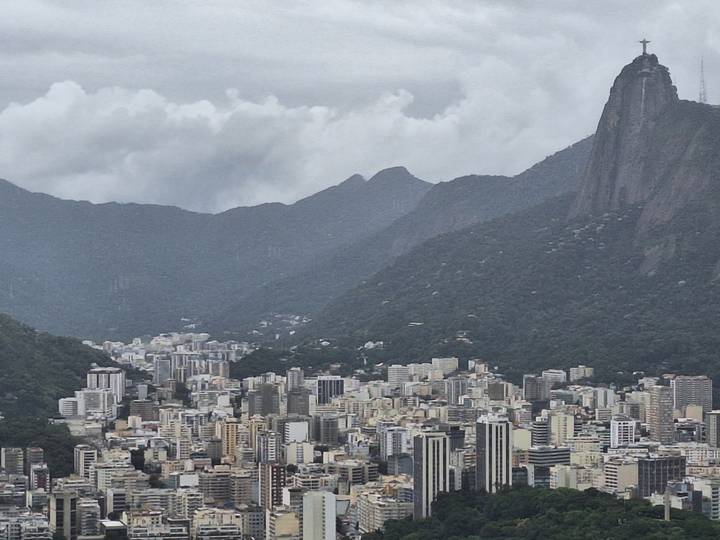 Wide cityscape of Rio de Janeiro with dense buildings below forested mountains under cloudy sky