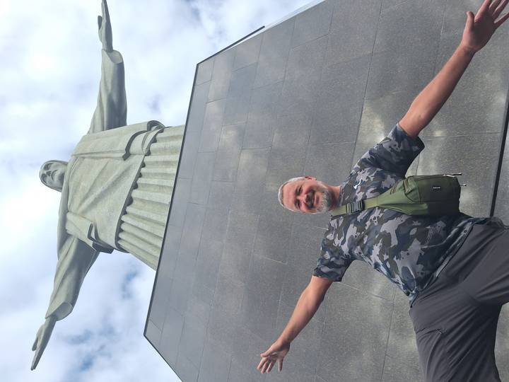 Man posing with arms outstretched at the base of Christ the Redeemer statue looking upward