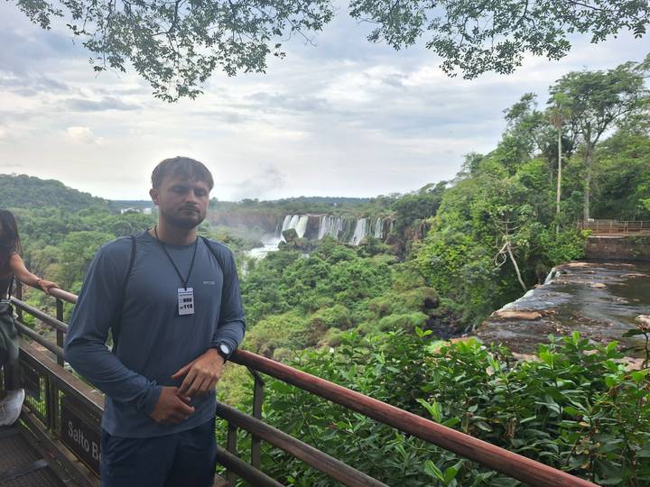 Young man stands at balcony viewpoint overlooking the powerful waterfalls and lush jungle of Iguazu