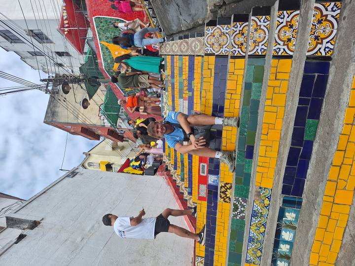 Traveller sits on colorful tiled steps of Selaron staircase surrounded by other visitors