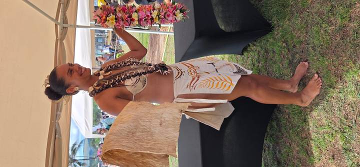 Smiling dancer wearing lei and traditional attire presents flower garland at outdoor event