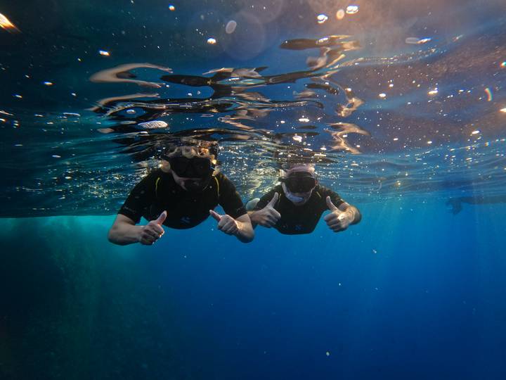 Two snorkelers give thumbs up underwater in clear blue sea