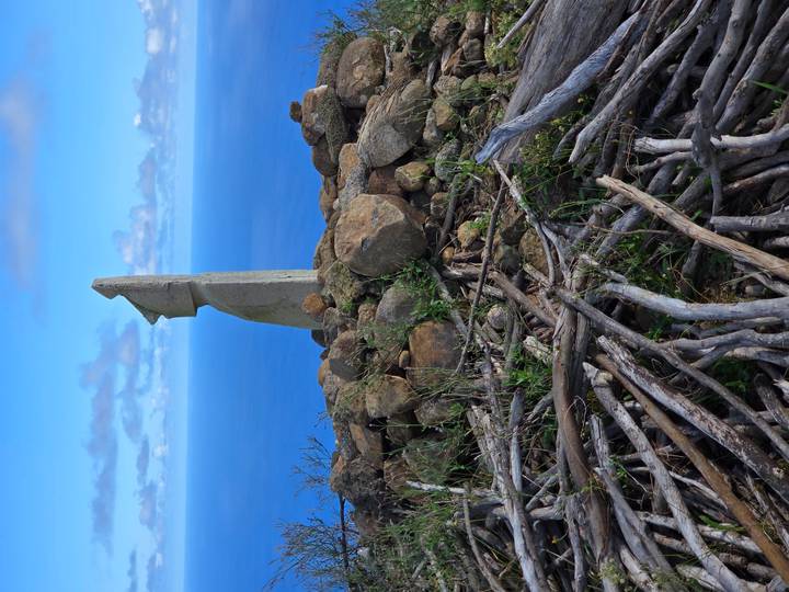 Modern stone sculpture resembling a Moai stands on rocky cairn overlooking vast ocean